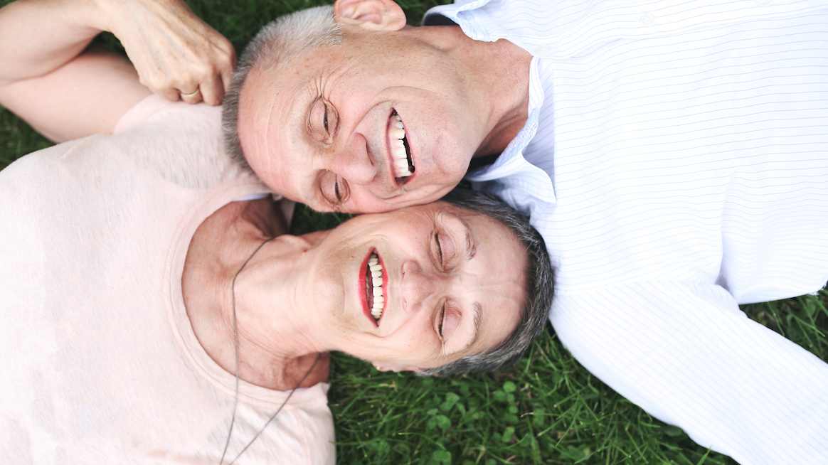 two-older-people-recline-on-grass-laughing-resilience-optimism-increase-with-age